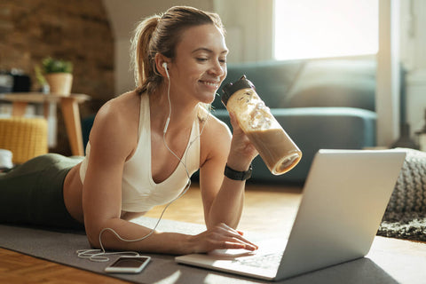 A woman drinking a protein shake while using a laptop.